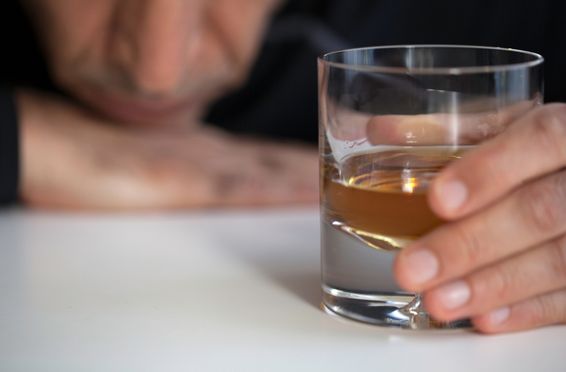 alcoholic man drinking whiskey at home struggling with the signs and symptoms of alcoholism