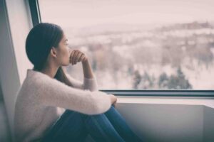 woman-experiencing-depression-looking-out-window Woman sitting by window reflecting during struggle with depression