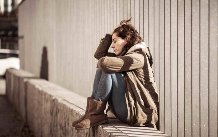 Woman sitting alone outdoors against a wall, representing the emotional impact behind Pennsylvania substance abuse statistics