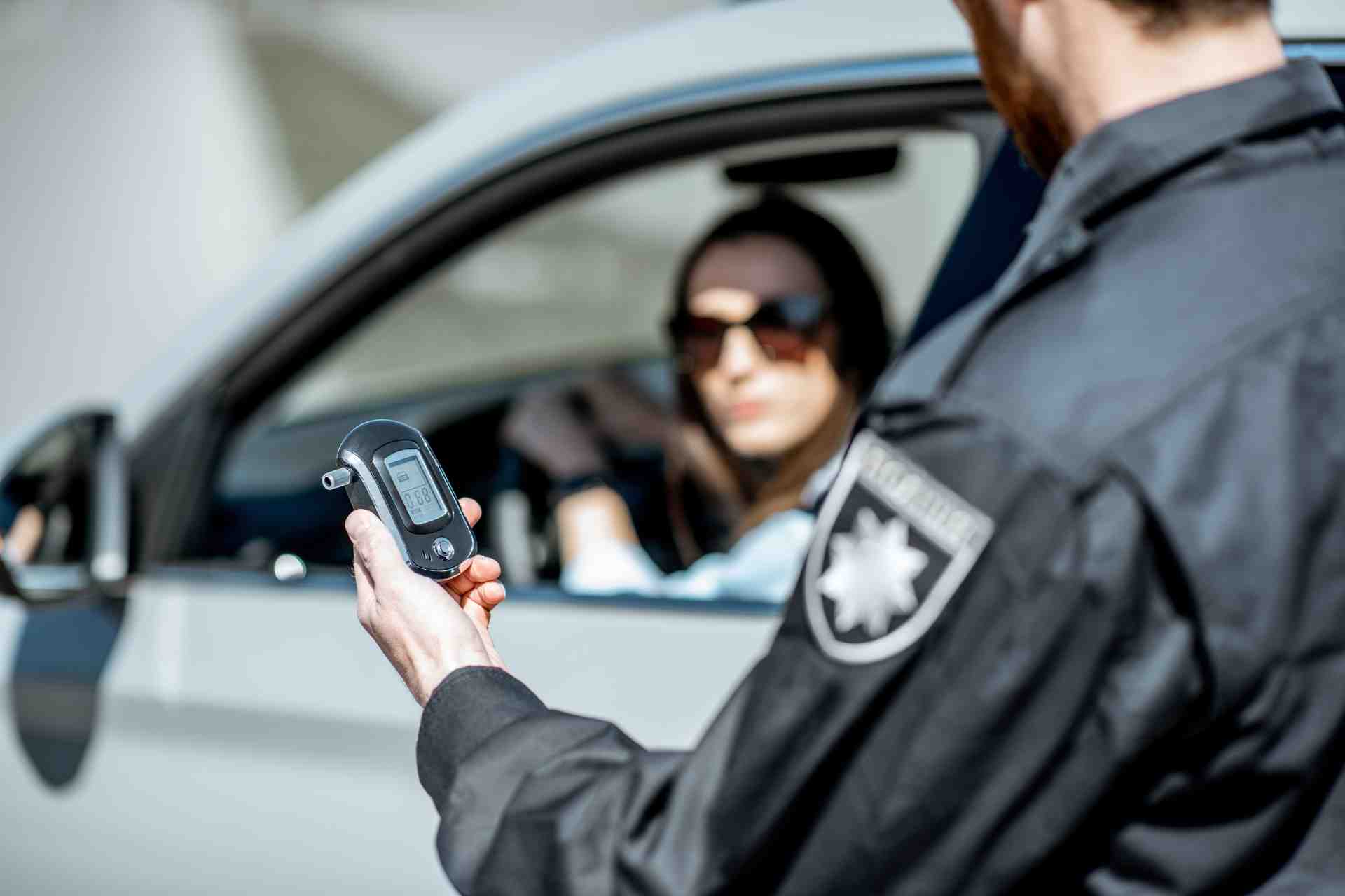 Police officer holding a breathalyzer device during a roadside DUI stop with a driver seated inside the car