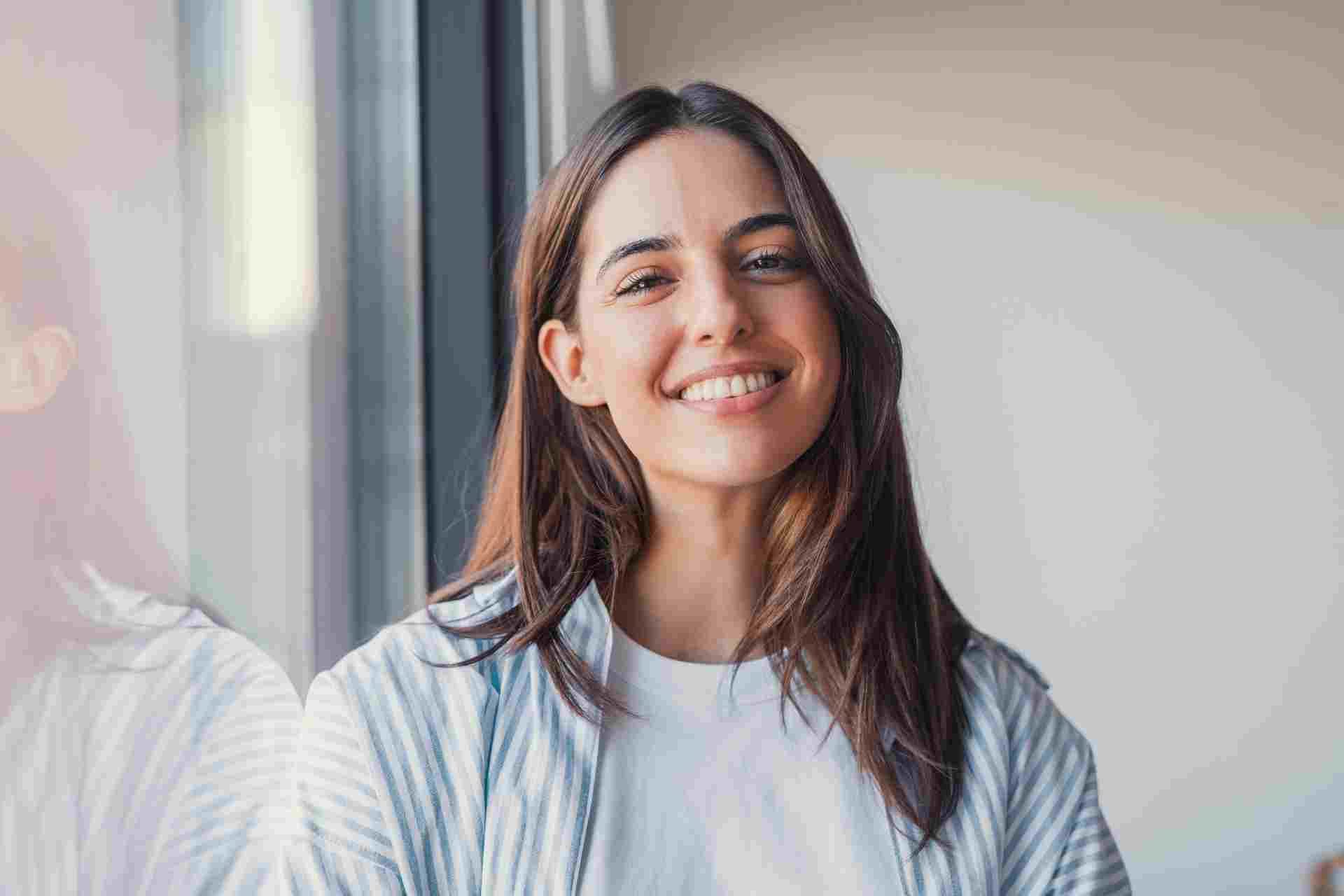 how long does drug detox take Smiling woman standing near a window representing stability and recovery following medically supervised drug detox.